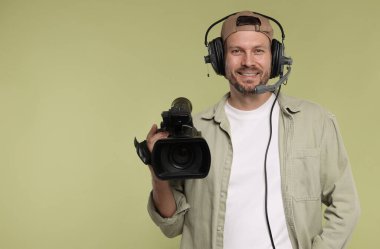 Profesyonel kamera ve soluk zeytinli arka planda kulaklığı olan bir adam.