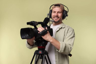 Profesyonel kamera ve soluk zeytinli arka planda kulaklığı olan bir adam.