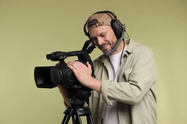 Profesyonel kamera ve soluk zeytinli arka planda kulaklığı olan bir adam.