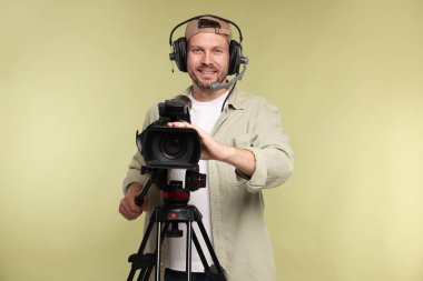 Profesyonel kamera ve soluk zeytinli arka planda kulaklığı olan bir adam.