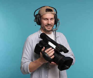 Profesyonel video kamerası ve açık mavi arka planda kulaklığı olan bir adam.