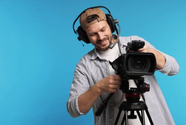 Açık mavi arka planda profesyonel video kamerası ve kulaklığı olan adam, metin için boşluk