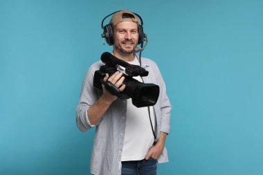 Profesyonel video kamerası ve açık mavi arka planda kulaklığı olan bir adam.