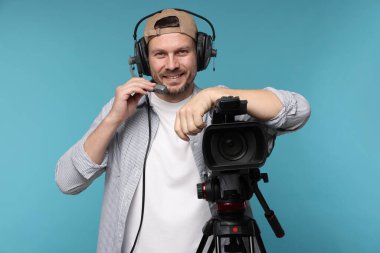 Profesyonel video kamerası ve açık mavi arka planda kulaklığı olan bir adam.