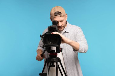 Açık mavi arka planda profesyonel video kamerası olan adam.