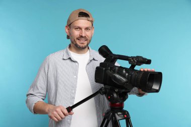 Açık mavi arka planda profesyonel video kamerası olan adam.