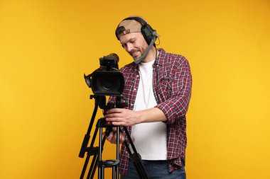 Profesyonel kamera ve turuncu arka planda kulaklığı olan bir adam.