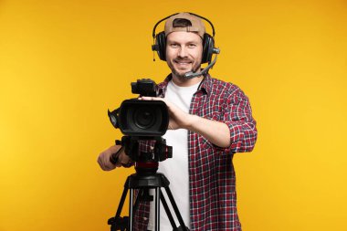 Profesyonel kamera ve turuncu arka planda kulaklığı olan bir adam.
