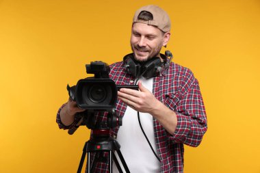 Profesyonel kamera ve turuncu arka planda kulaklığı olan bir adam.