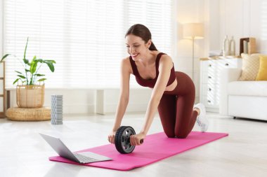 Evde dizüstü bilgisayarla video öğretirken karın kaslarıyla egzersiz yapan mutlu kadın.