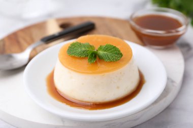 Beyaz mermer masada servis edilen karamel soslu lezzetli puding, yakın plan.