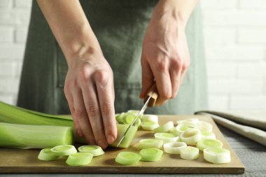 Gri ahşap masada pırasa kesen kadın, yakın plan.