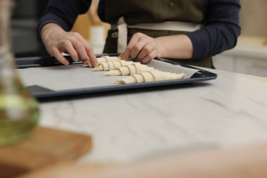 Beyaz masadaki pişirme örtüsüne çiğ kruvasan koyan kadın, yakın plan.