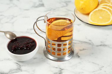 Metal tutacakta bir bardak çay, reçel ve limon dilimleri beyaz mermer masada, yakın plan.