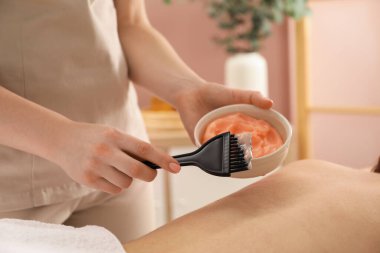 Vücut sargısı için kozmetik ürünler uygulayan estetikçi kaplıca salonundaki kadının sırtına sarıp kapatıyor.