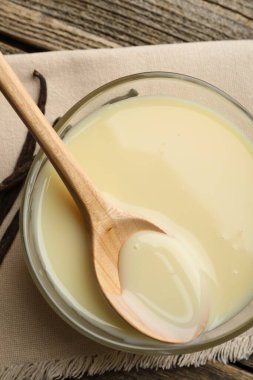 Yoğun süt, kaşık ve vanilya kapsülleri ahşap masada, düz yerde.