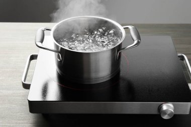 Kaynar suyla pişirme tenceresi ve ahşap masa üzerinde gri arka plan, yakın çekim