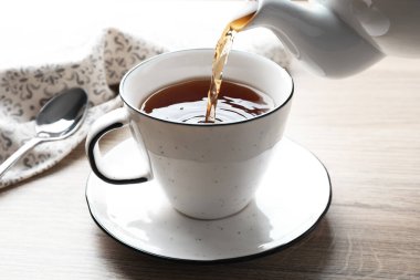 Tahta masada çaydanlıktan fincana taze demlenmiş çay dökülüyor, yakın plan.