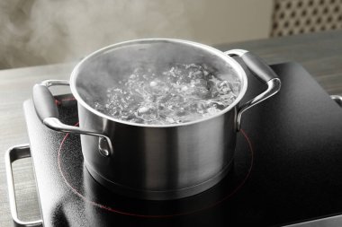 Kaynar suyla pişirme tenceresi ve ahşap masa üzerinde gri arka plan, yakın çekim