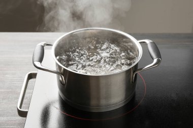 Kaynar suyla pişirme tenceresi ve ahşap masa üzerinde gri arka plan, yakın çekim