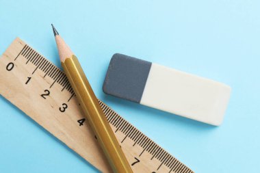 Açık mavi arkaplanda silgi, kalem ve cetvel, üst görünüm