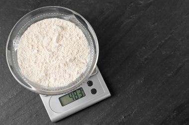 Elektronik mutfak terazisi, koyu dokulu masa üzerinde bir kase un, üst manzara. Metin için boşluk