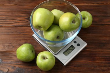 Elektronik mutfak terazisi ve ahşap masada bir kase yeşil elma.