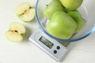 Elektronik mutfak terazisi, beyaz ahşap masada yeşil elma kasesi, düz.