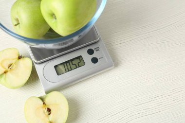 Elektronik mutfak terazisi ve beyaz ahşap masada bir kase yeşil elma. Metin için boşluk