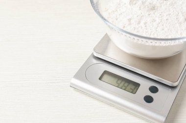 Elektronik mutfak terazisi ve beyaz ahşap masa üzerinde bir kase un, yakın plan. Metin için boşluk
