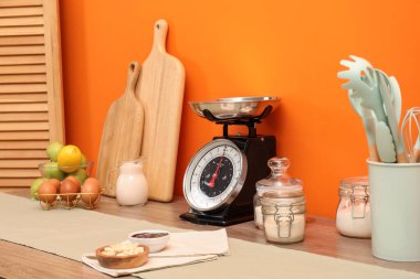 Kitchen scale, products and cooking utensils on wooden table