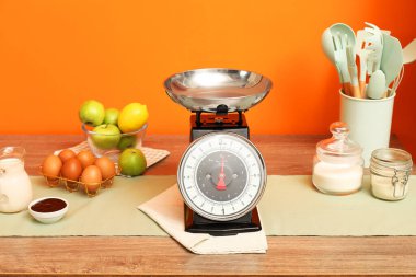 Kitchen scale, products and cooking utensils on wooden table
