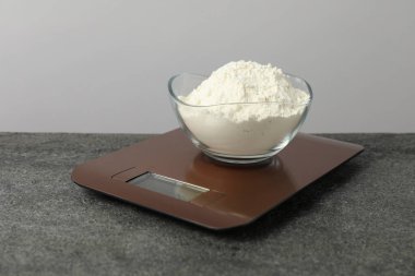 Modern elektronik mutfak terazisi, gri masa üzerinde bir kase un, yakın plan.