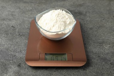 Modern elektronik mutfak terazisi, gri masa üzerinde bir kase un, yakın plan.