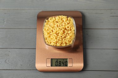 Modern elektronik mutfak terazisi. Gri ahşap masa üzerinde bir kase çiğ makarna.