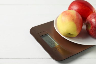 Modern electronic kitchen scale with apples on white wooden table, closeup. Space for text