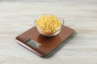 Modern elektronik mutfak terazisi, ahşap masada çiğ makarna, yakın plan.