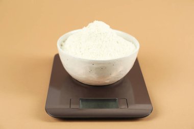 Elektronik mutfak terazisi, bej arka planda bir kase un, yakın plan.