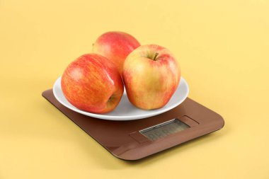 Electronic kitchen scale with apples on yellow background, closeup