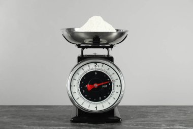 Mechanical kitchen scale with bowl of flour on dark textured table against grey background