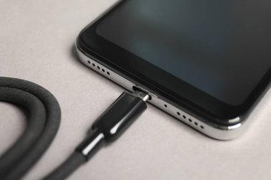Açık gri arkaplanda akıllı telefona bağlı USB şarj kablosu, kapat