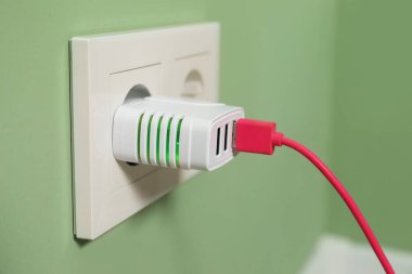 Açık yeşil duvardaki elektrik prizine bağlı USB adaptörüName