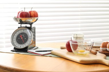 Retro mekanik mutfak ölçeği, ürünler ve ahşap masa üzerindeki kırtasiye.