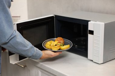 Yemek tabağını mikrodalgaya koyan adam, yakın plan.