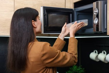 Kadın, yemeğiyle birlikte mikrodalgayı içine koyuyor.