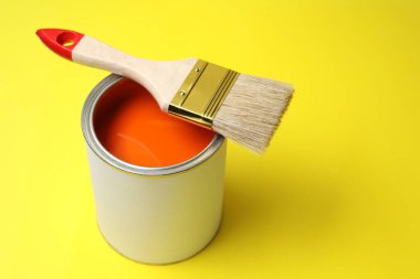 Can of orange paint and brush on yellow background