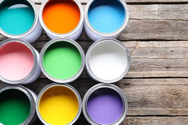 Cans of bright paints on wooden table, flat lay. Space for text