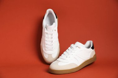 Pair of stylish sneakers on red-brown background. Casual shoes