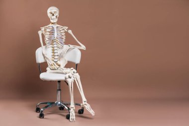 Açık kahverengi arkaplan üzerinde oturan yapay insan iskelet modeli, metin için boşluk