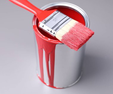 Can of red paint and brush on grey background, closeup